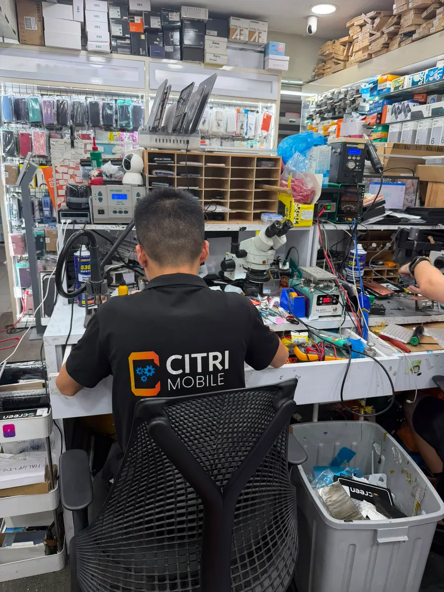 Citri Mobile technician at the Chinatown phone repair bench, lined with spare parts and screen protectors